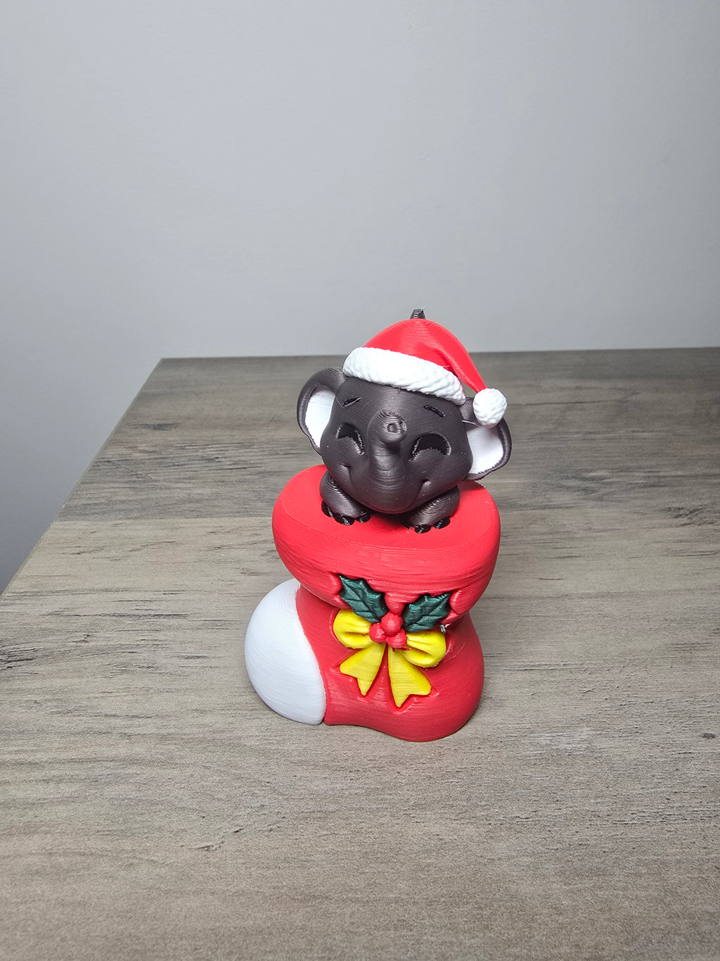 Digitally painted elephant Christmas ornament wearing a Santa hat and peeking from a red stocking