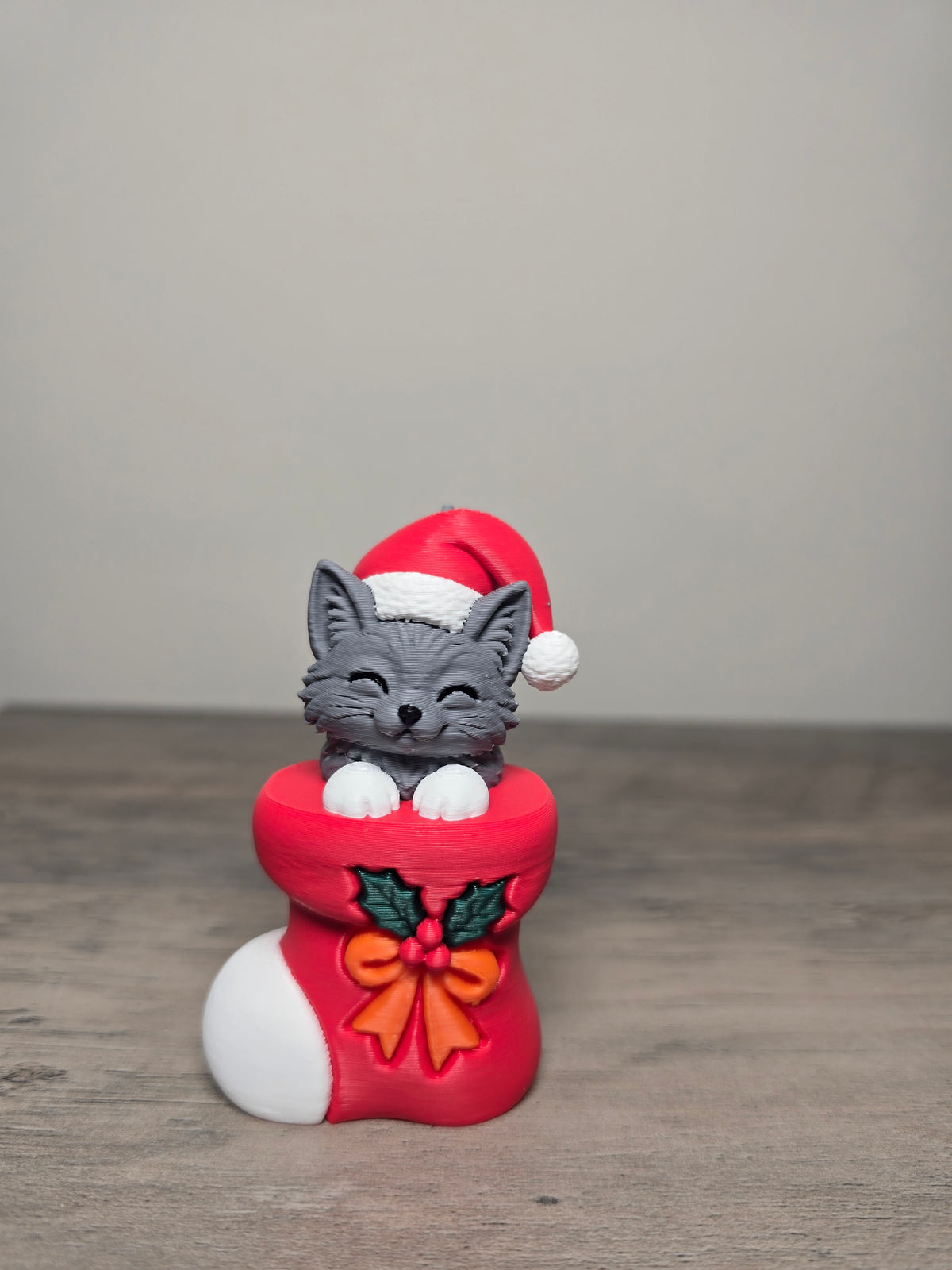 Digitally painted gray long-haired kitten Christmas ornament wearing a Santa hat in a red stocking