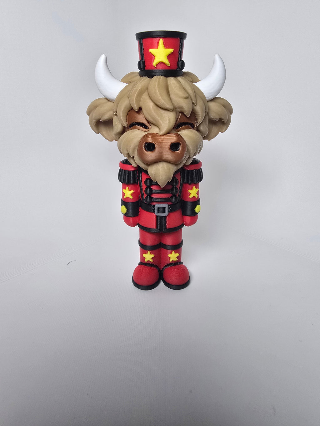 Highland cow nutcracker figurine in a red and black uniform with yellow stars and white horns