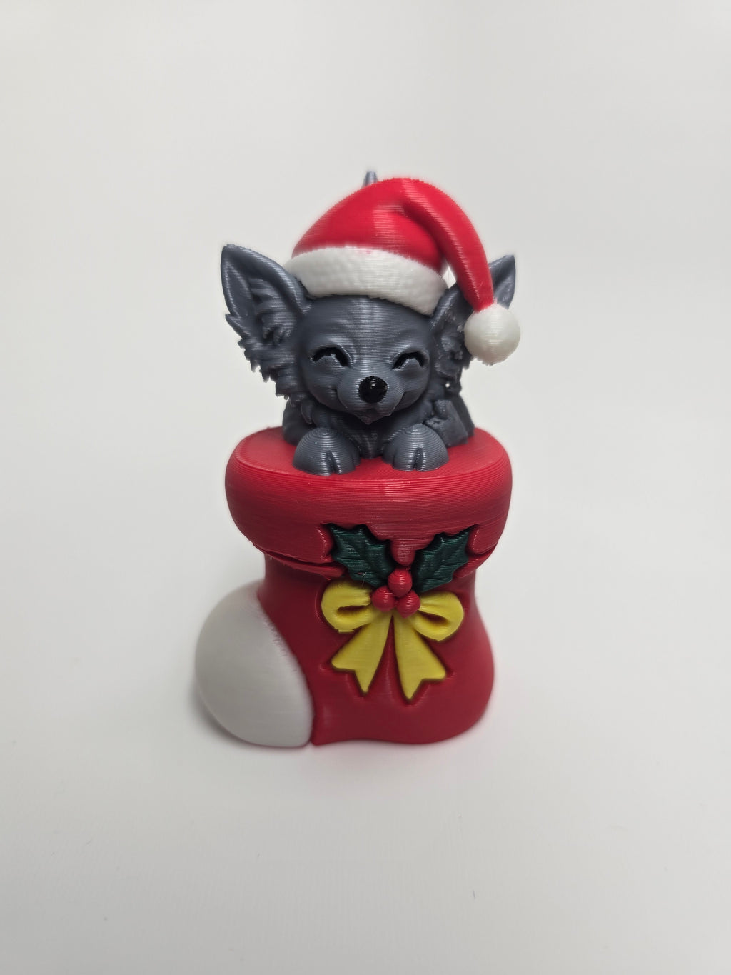 Long-haired Chihuahua wearing a Santa hat in a red Christmas stocking with holly and yellow bow
