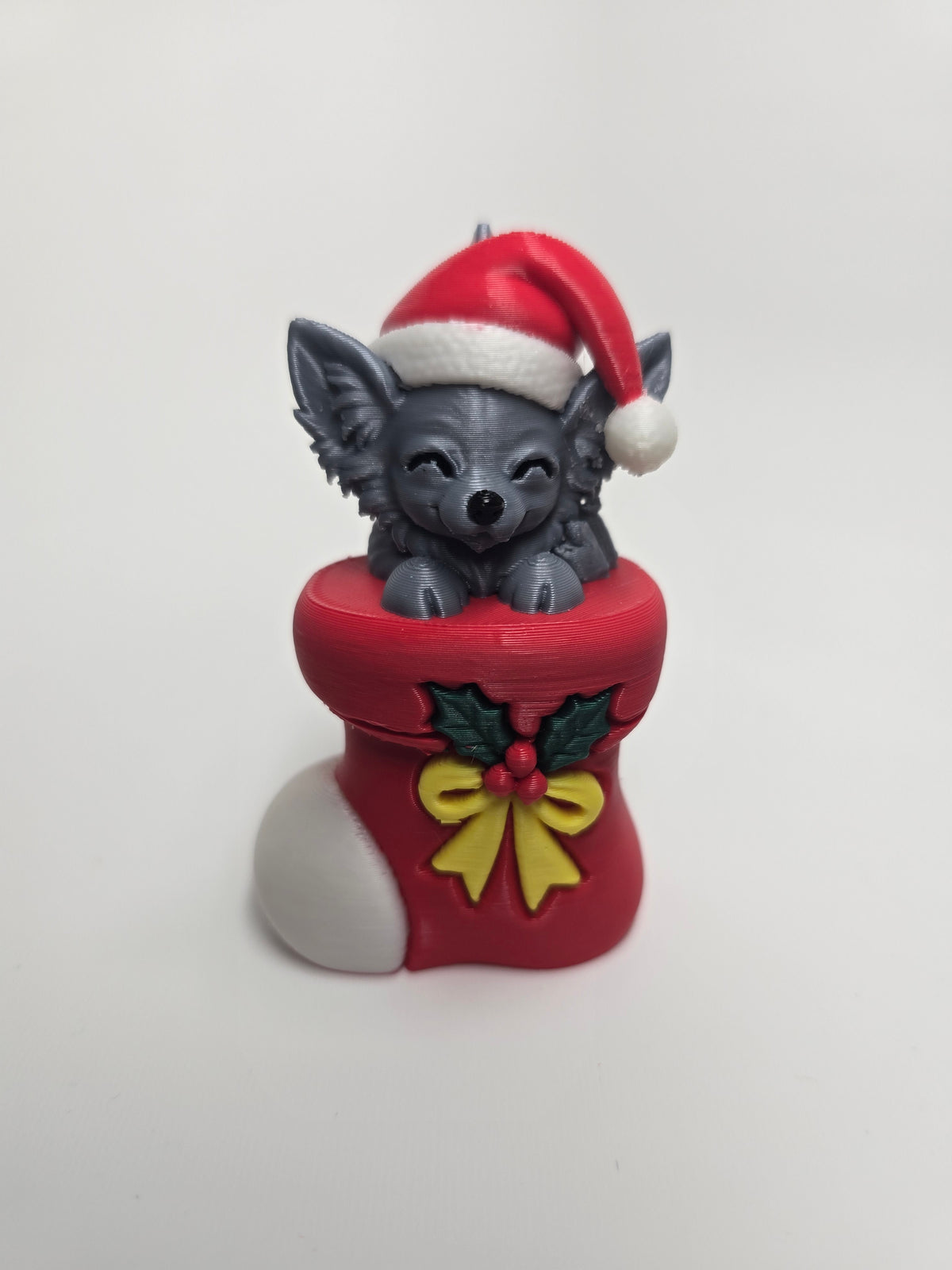 Long-haired Chihuahua wearing a Santa hat in a red Christmas stocking with holly and yellow bow