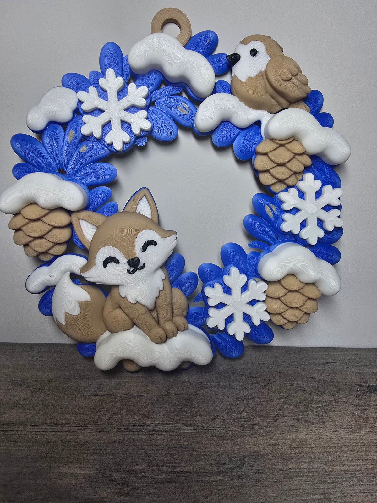 Blue woodland winter wreath with a fox, bird, white snowflakes, and snow-topped pinecones