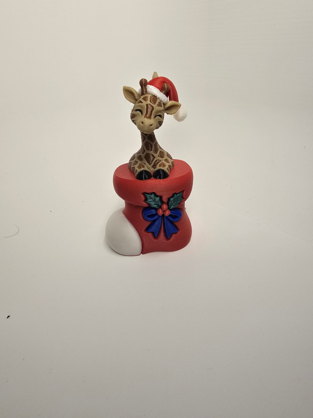 Giraffe wearing a Santa hat in a red Christmas stocking with holly and a blue bow