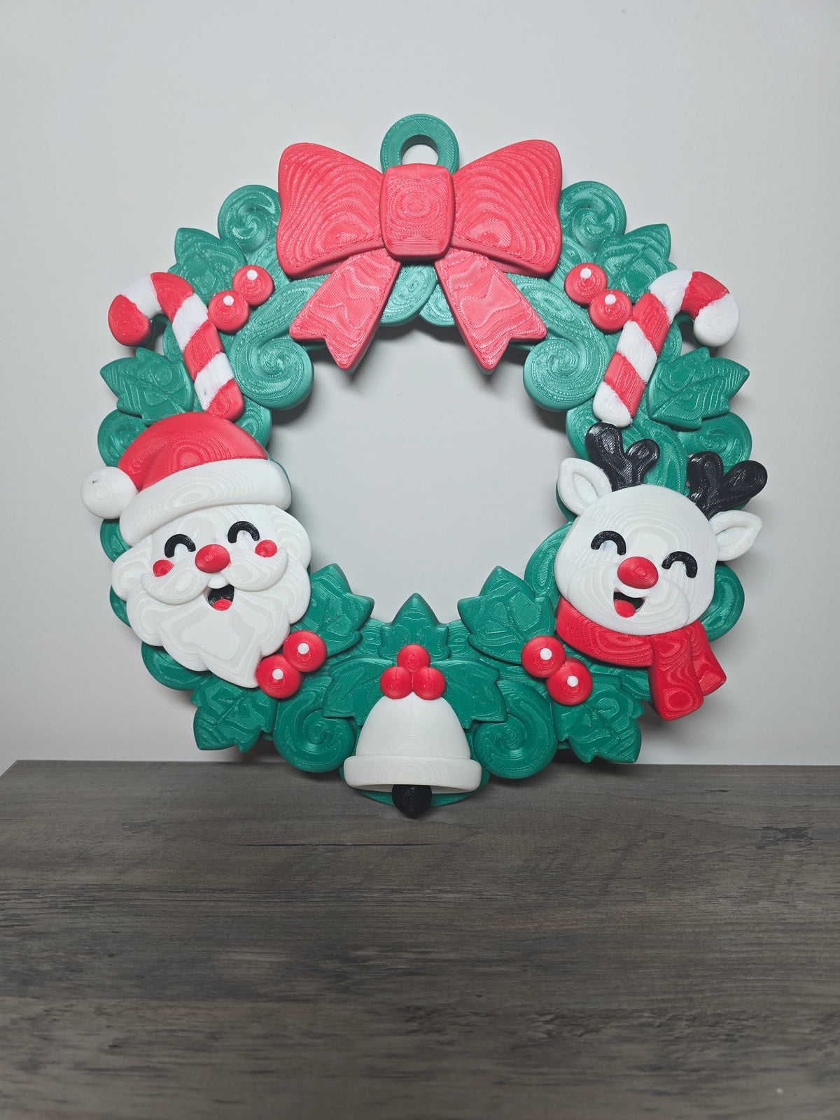 3D printed Christmas wreath with Santa, a smiling reindeer, candy canes, green foliage, a white bell, and a red bow