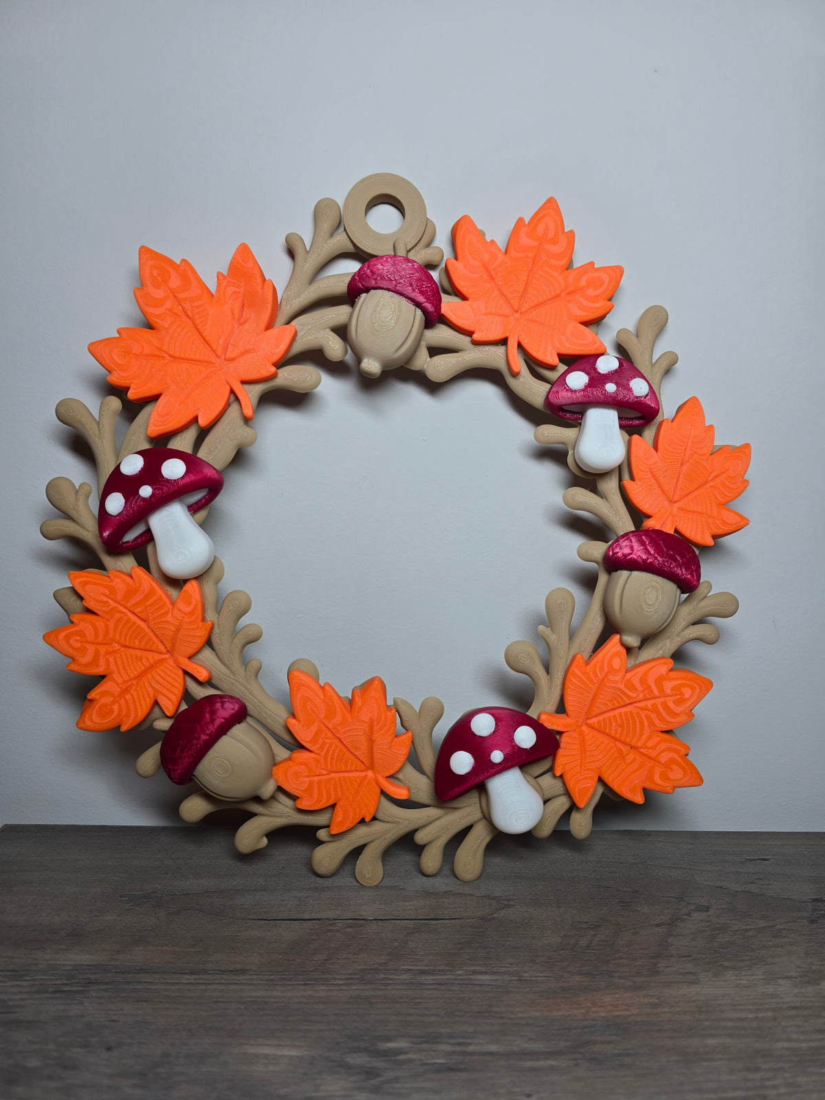Fall wreath with orange leaves, burgundy-capped acorns, and spotted mushrooms on a branching wood-toned frame