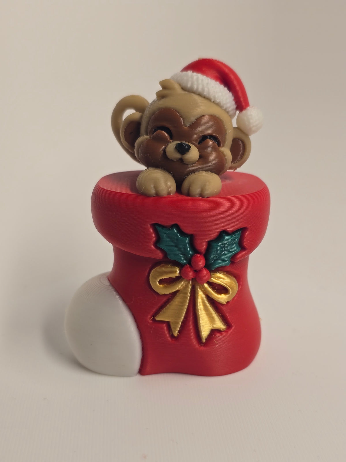 Smiling monkey in a Santa hat peeking from a red Christmas stocking decorated with holly, berries, and a golden bow